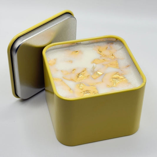 Square candle in a yellow tin with a white interior on a light gray background